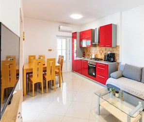 A modern kitchen with red cabinets, a dining area with wooden chairs, and a glass coffee table. - Apartments Foric (Rab)