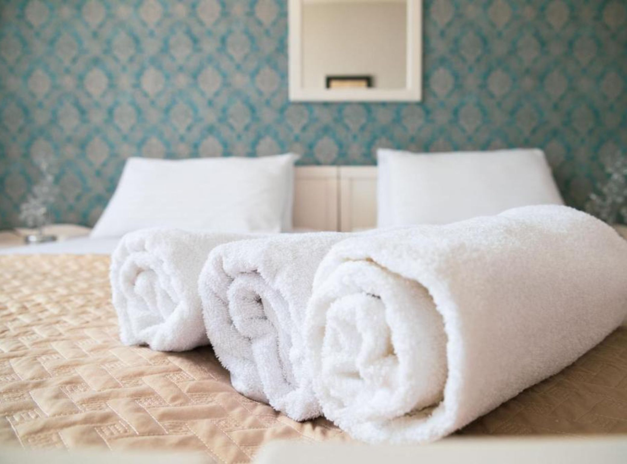 A neatly made bed with a beige quilt and two rolled white towels.