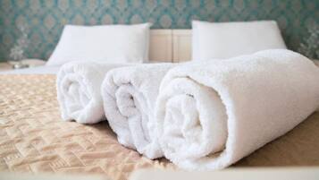 A neatly made bed with a beige quilt and two rolled white towels.