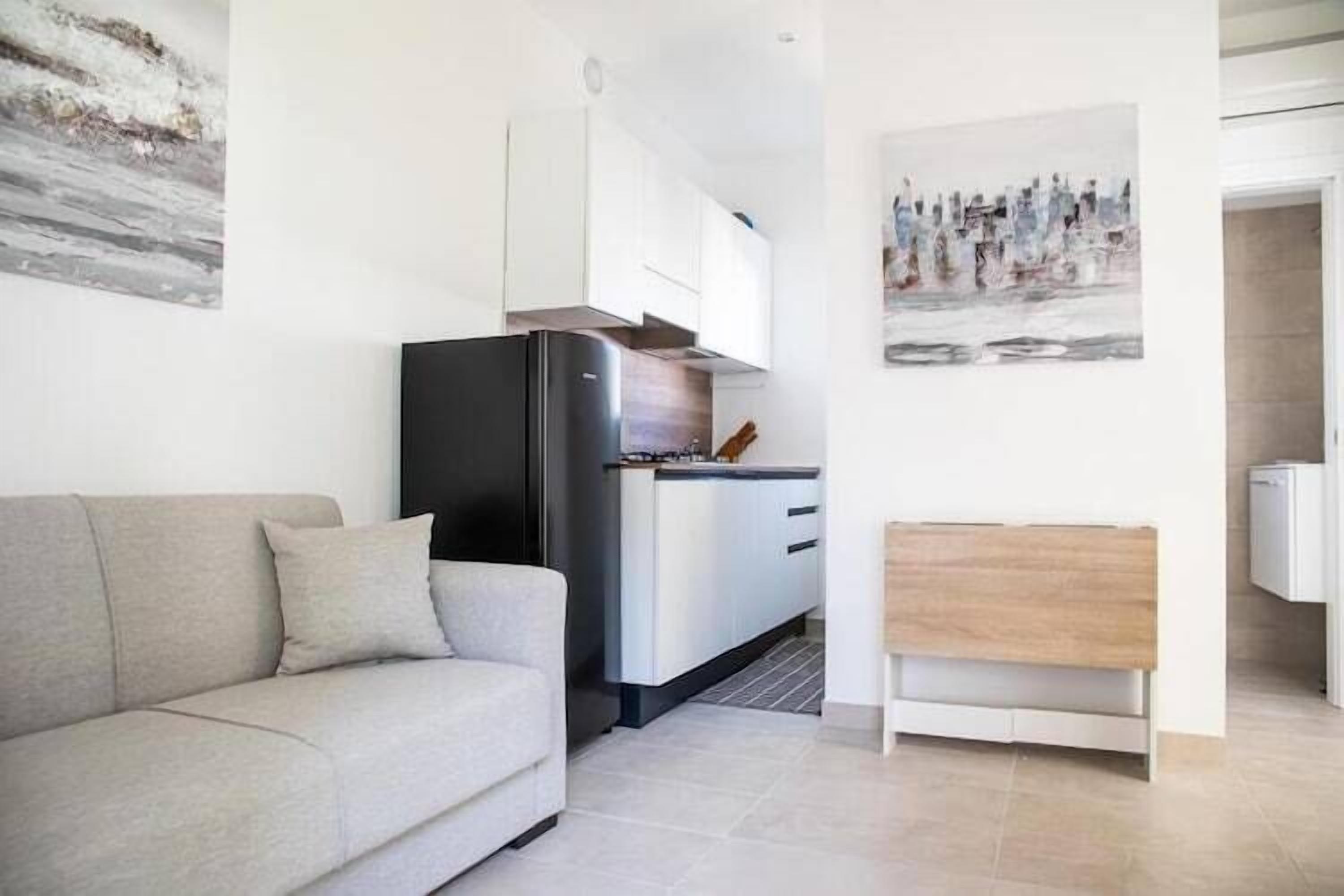 Een moderne woonkamer met een bank, een keukenhoek met een koelkast, en een houten bijzettafeltje.