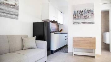 Een moderne woonkamer met een bank, een keukenhoek met een koelkast, en een houten bijzettafeltje.