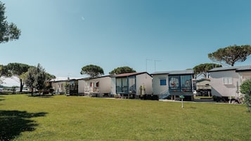 Een rij gelijkvloerse huizen met een gazon ervoor, elk met een klein portaaltje en een raam.