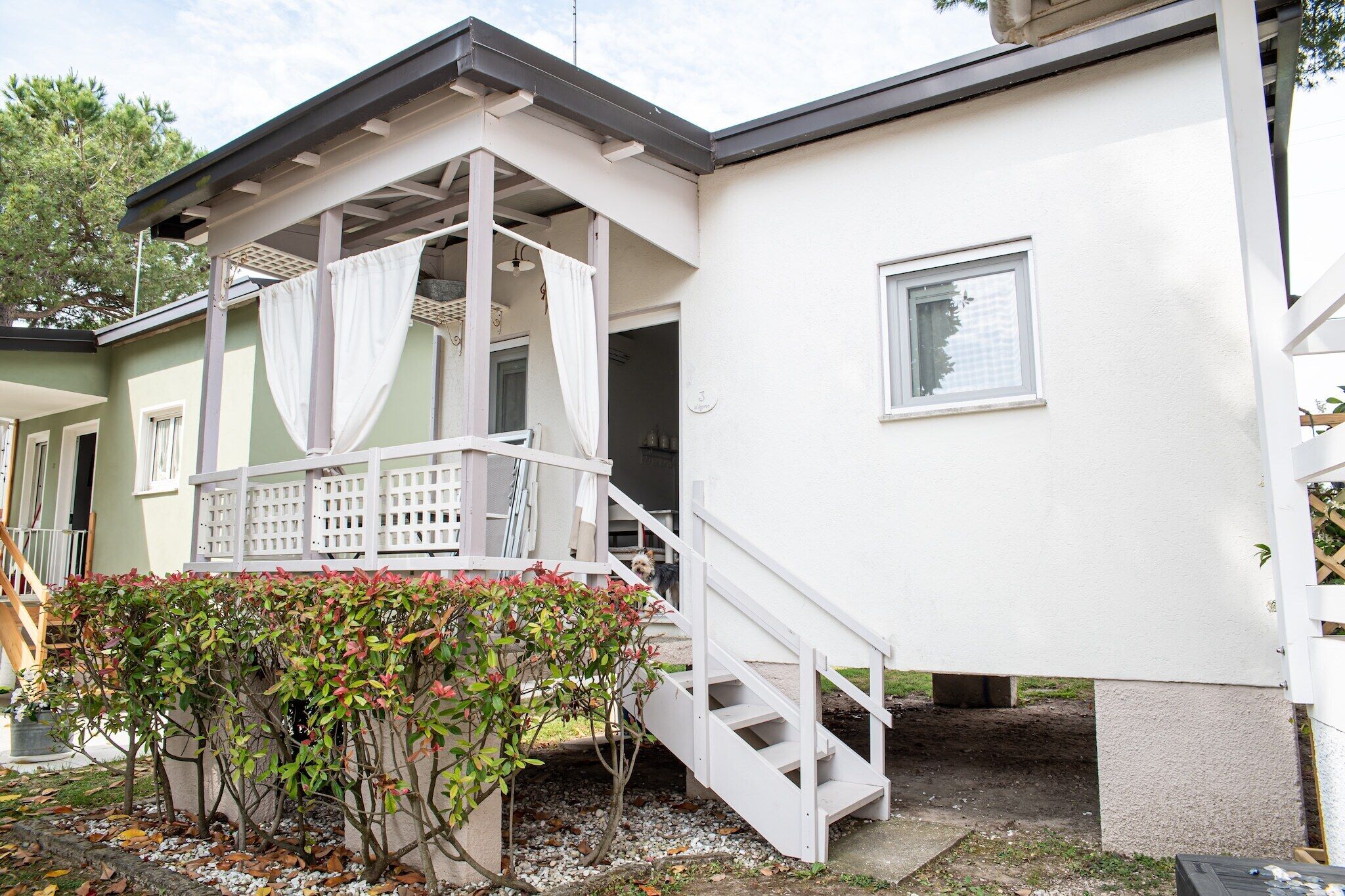 Une maison dotée d’un porche abrité, d’un escalier menant à l’entrée et d’un petit jardin agrémenté d’arbustes.