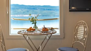 A room with a view of the sea, a table with pastries, a vase with flowers, and two chairs.