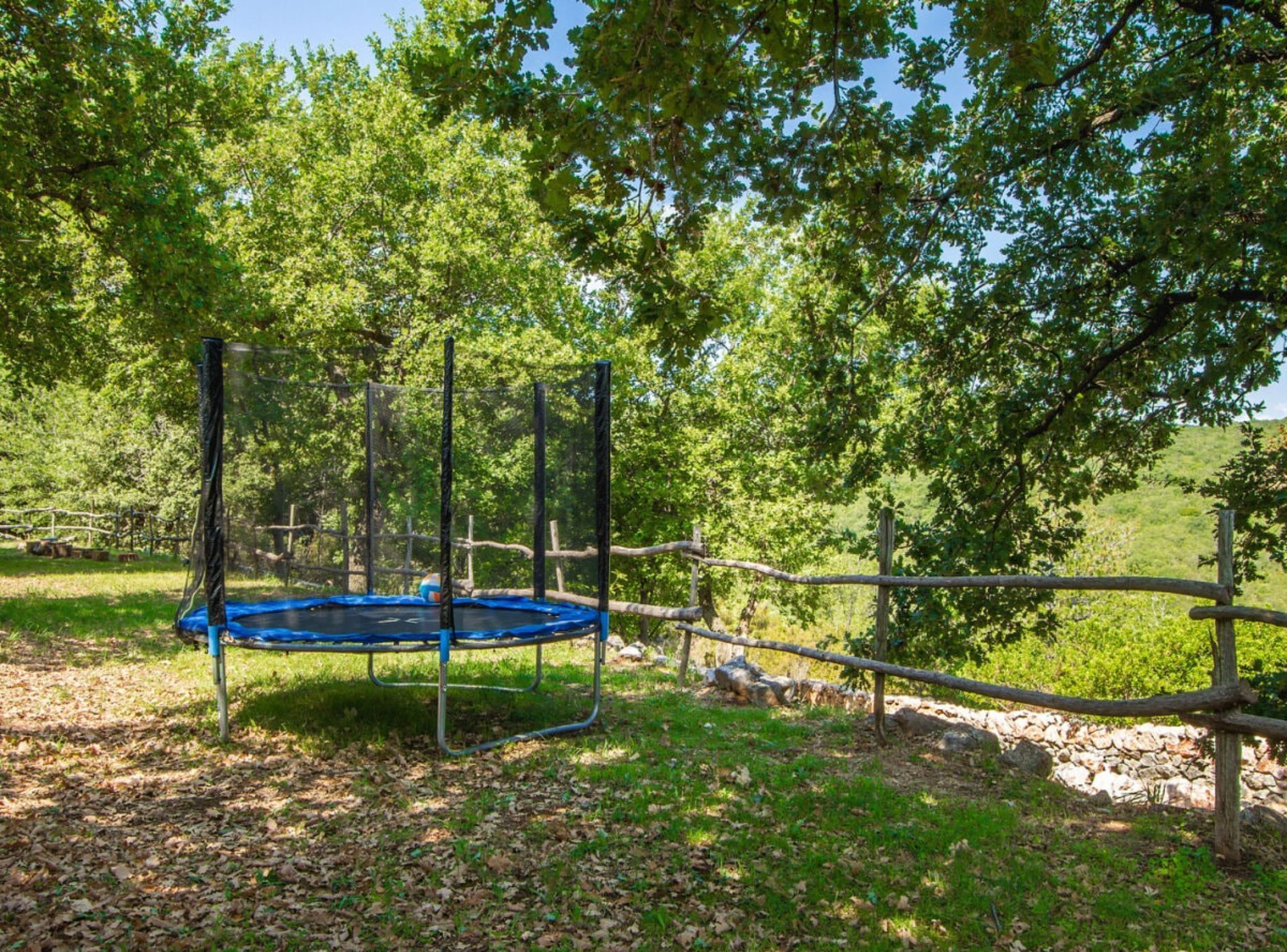 A trampoline in a wooded area with a fence and trees.