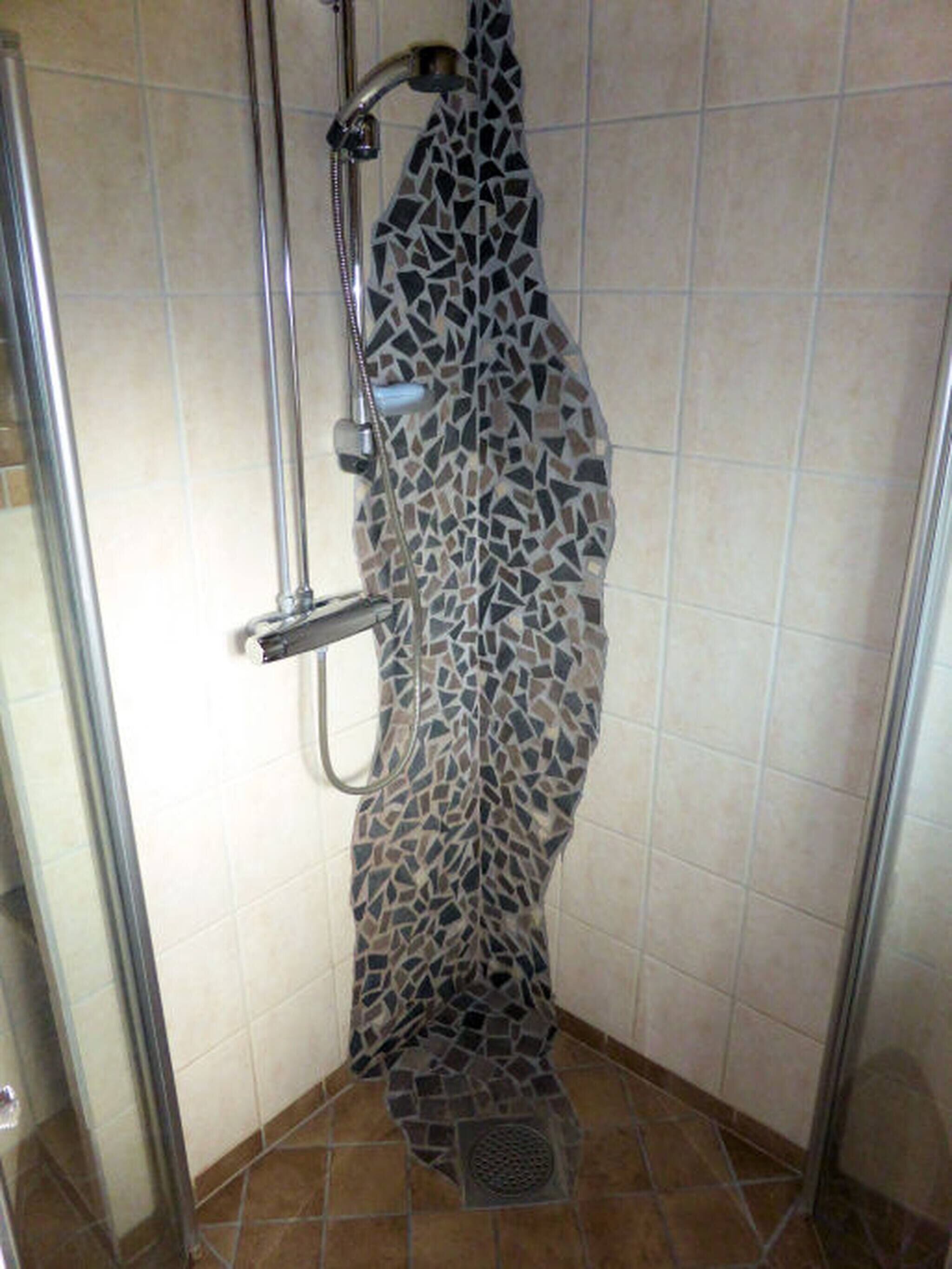Et brusebad med væg i mosaikfliser og et metal brusehoved.