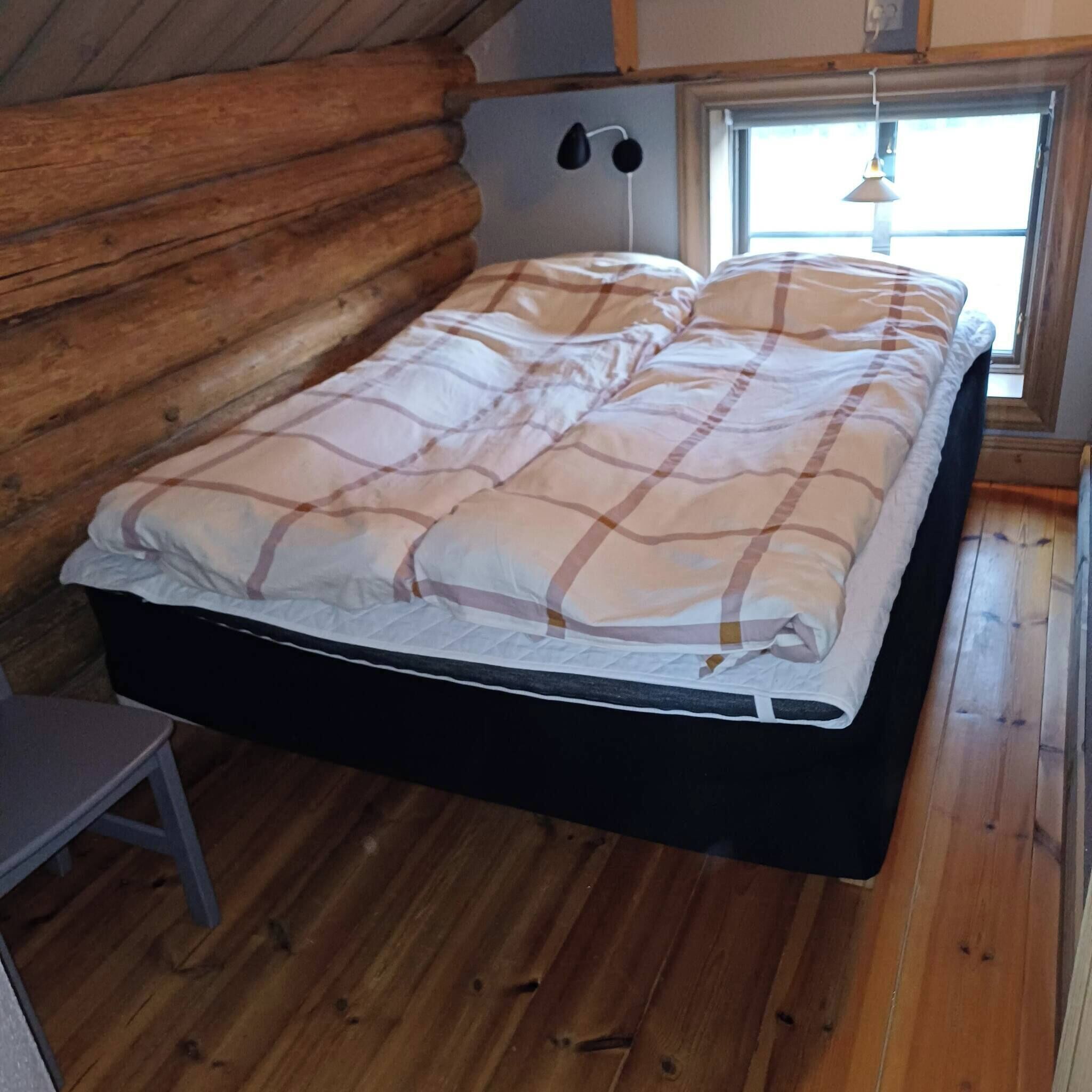 Ett sovrum i en timmerstuga med en säng, ett litet bord och ett fönster med utsikt.