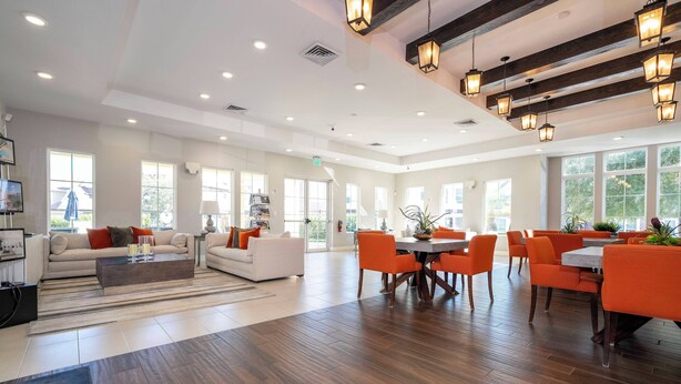 A spacious hotel lobby with a modern design, featuring a seating area with orange chairs and a white sofa, a dining area with a round table, and large windows allowing natural light. - Sunny Dreams Vacation Home 3 miles to Disney 7574 (Kissimmee)