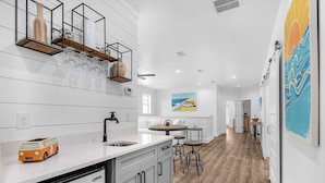 A modern kitchen with a white countertop, a built-in dishwasher, and a dining area with a round table and bar stools. - Latitude! New! 8 Bed! Beach! (Destin)