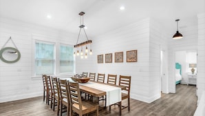 A dining area with a wooden table and chairs, a hanging light fixture, and a window with blinds. - Latitude! New! 8 Bed! Beach! (Destin)