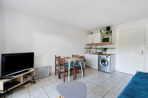 A compact living space with a TV, dining table, chairs, a washing machine, and a sofa. - Golf Pornic Apartment, Pool and Seaside! (Pornic)