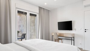 Una camera d'albergo con un letto, una scrivania, una sedia, una televisione e una porta-finestra scorrevole su un balcone.