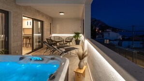 Un balcone con vasca idromassaggio, zona salotto e vista sulle montagne al crepuscolo.