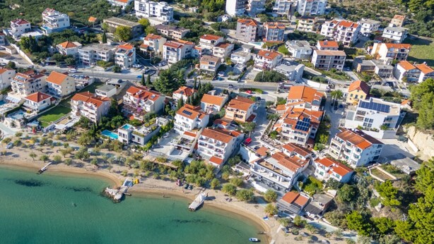 Vista aerea di una cittadina costiera con edifici residenziali, una spiaggia e barche.
