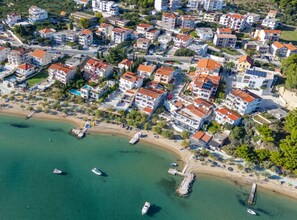 An aerial view of a coastal town with residential buildings, a beach, and boats. - Apartment Tomislav With Sea View and Hot-tub (Dugi Rat)