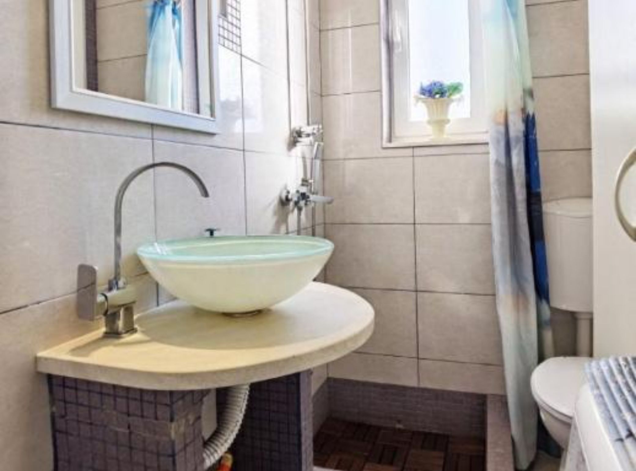 A bathroom with a large, round, light-colored sink, a mirror above it, and a window with a view of the outside.