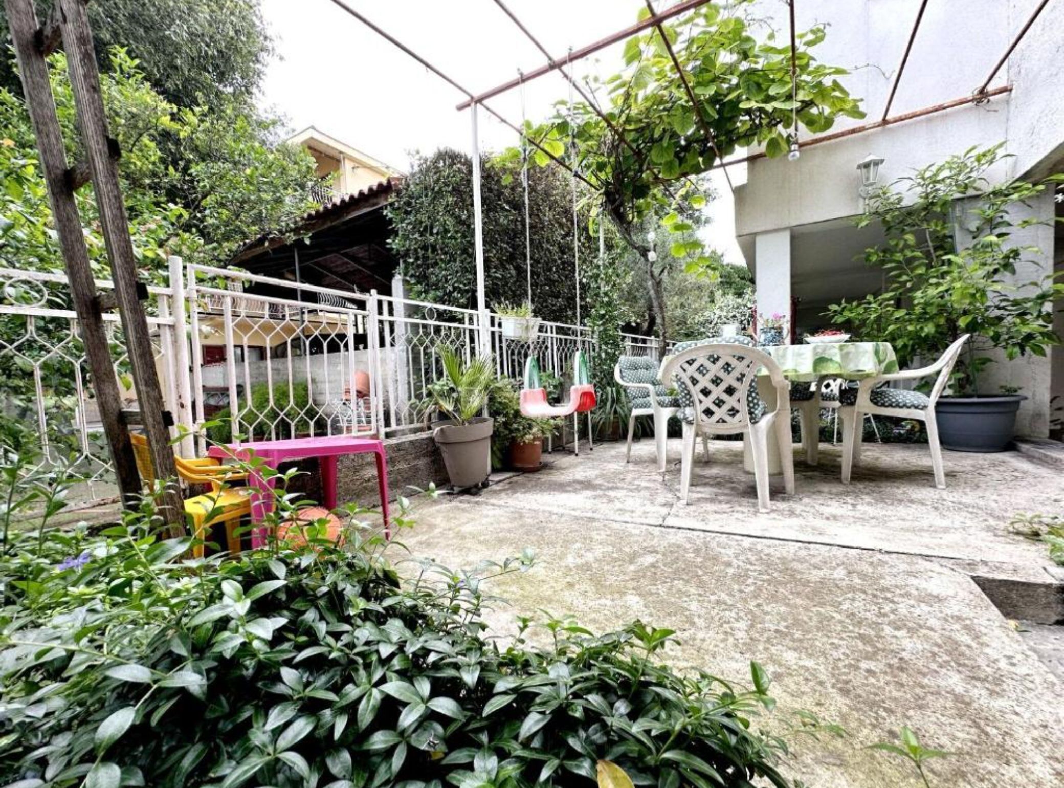 A patio area with a table and chairs, surrounded by potted plants and a white fence.