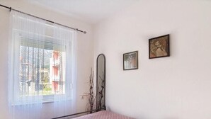 Makuuhuoneessa on sänky, ikkuna, jossa on läpikuultavat verhot, ja seinällä on kaksi kehystettyä kuvaa.