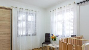 Une pièce avec un plancher en bois, une chaise noire, une petite table recouverte d’une nappe en dentelle et un berceau en bois.