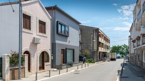 Une vue de rue avec des immeubles, dont un bâtiment à deux étages doté d’un balcon et un immeuble moderne avec de grandes fenêtres.