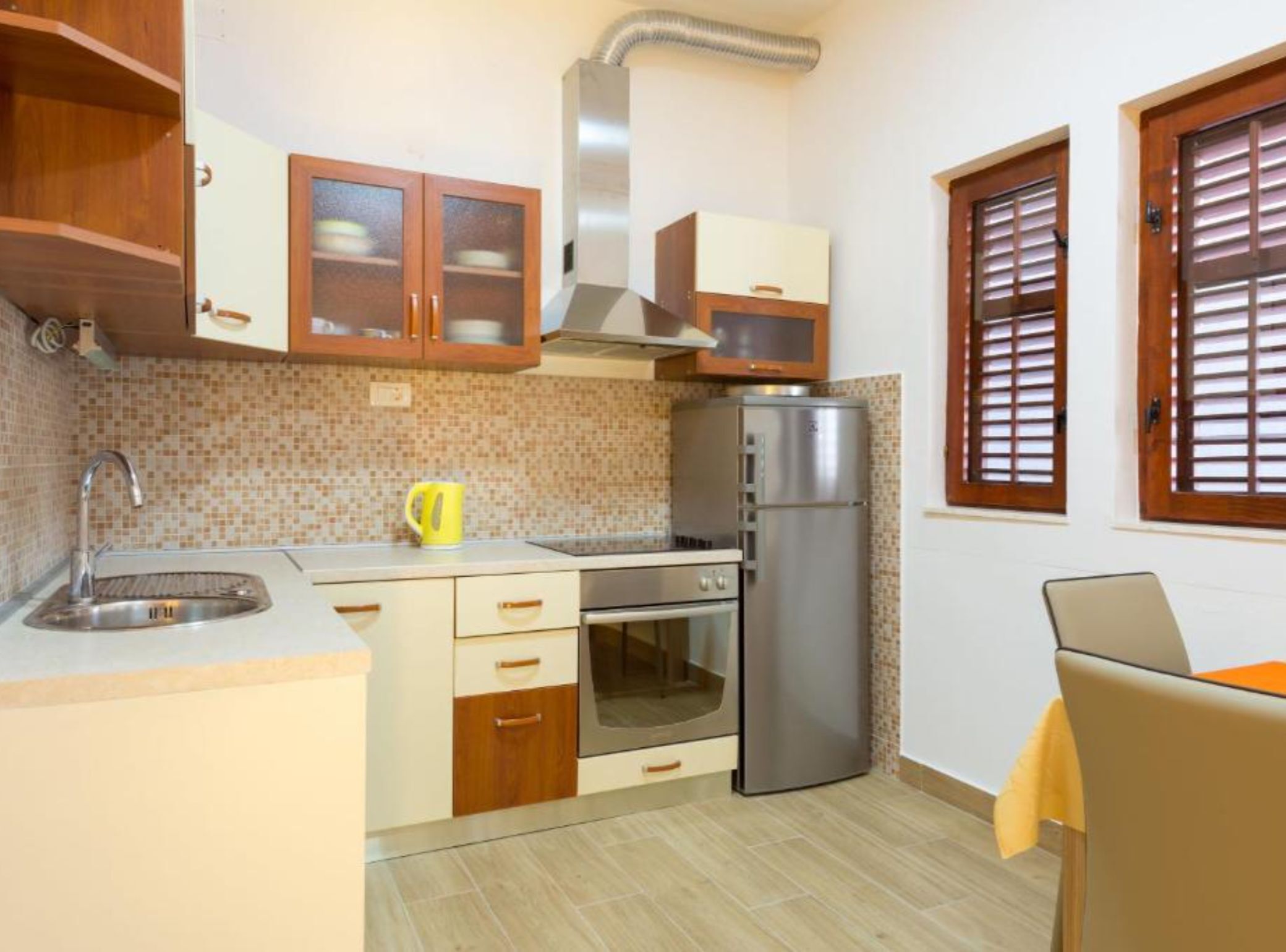 Cocina compacta con fregadero, estufa, horno y refrigerador. Cuenta con gabinetes de madera y una ventana con persianas.