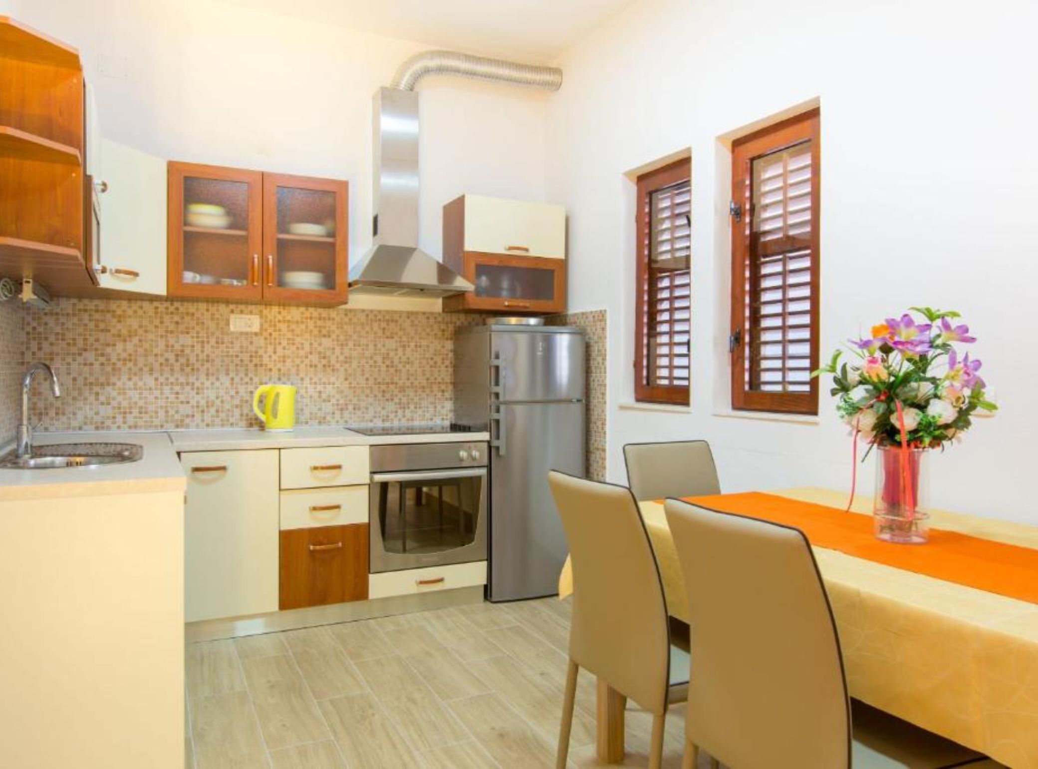 A compact kitchen with a refrigerator, oven, and microwave. There is a dining table with chairs and a vase of flowers.