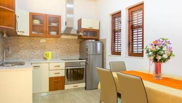 A compact kitchen with a refrigerator, oven, and microwave. There is a dining table with chairs and a vase of flowers.