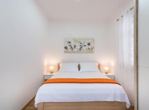 Une chambre à coucher avec un lit, deux tables de chevet, un tableau accroché au mur et une fenêtre avec des rideaux.