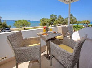 A balcony with wicker furniture, a table with breakfast items, and a view of the sea and trees. - Apartments Blue Horizon Retreat (Zadar)