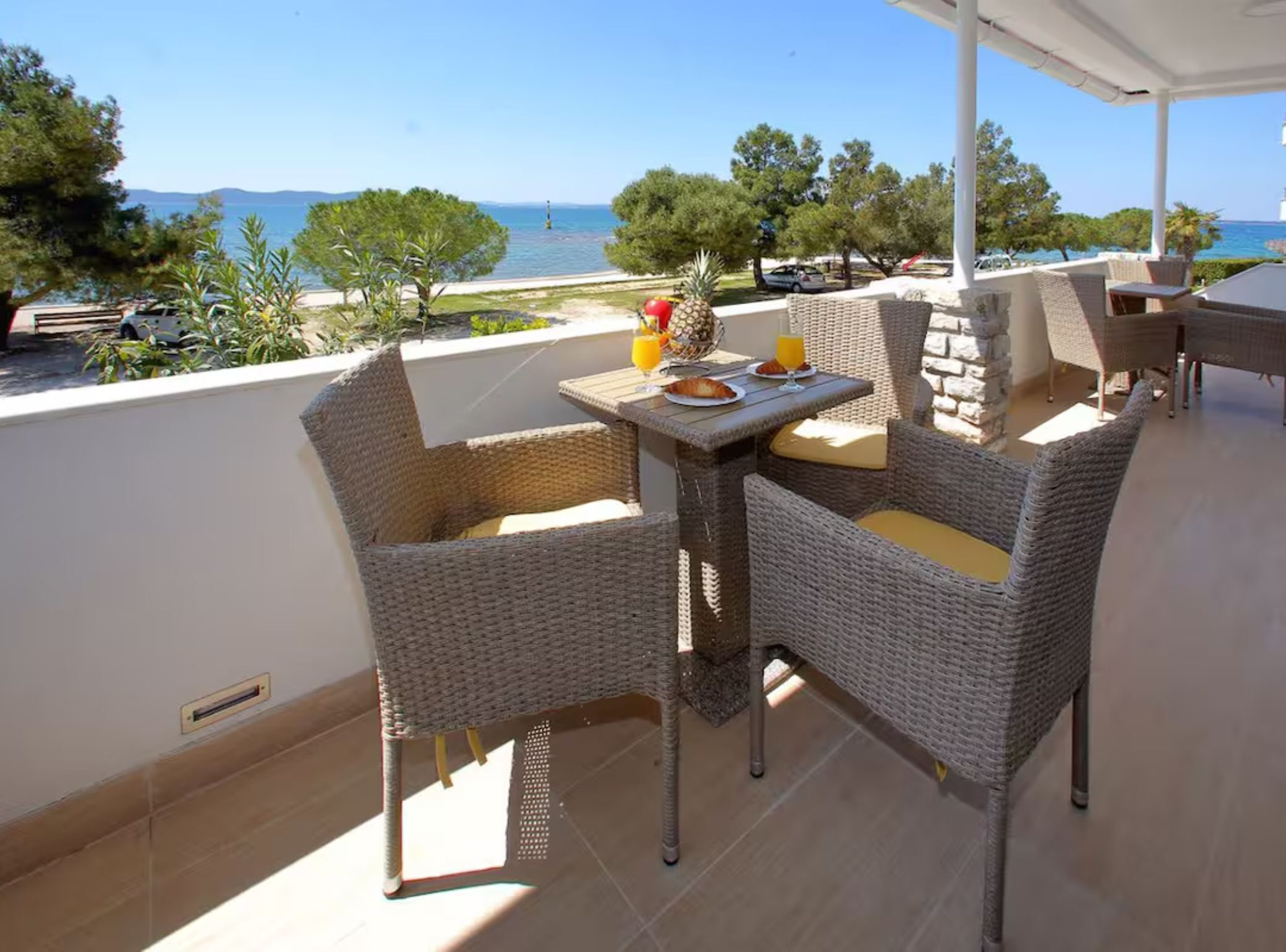 A balcony with wicker furniture, a table set with plates, glasses, and a pineapple.