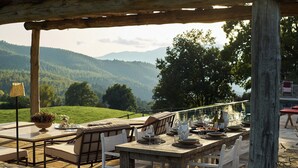 Ein Essbereich im Freien mit einem Holztisch, gedeckt für eine Mahlzeit, mit Blick auf eine malerische Berglandschaft.