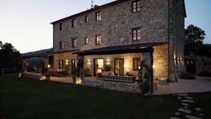 Ein Steinhaus mit überdachter Terrasse, mehreren Fenstern und Außenbeleuchtung.