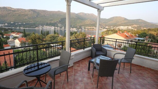 Un balcone con tavolo e sedie, vista su un lago e montagne.