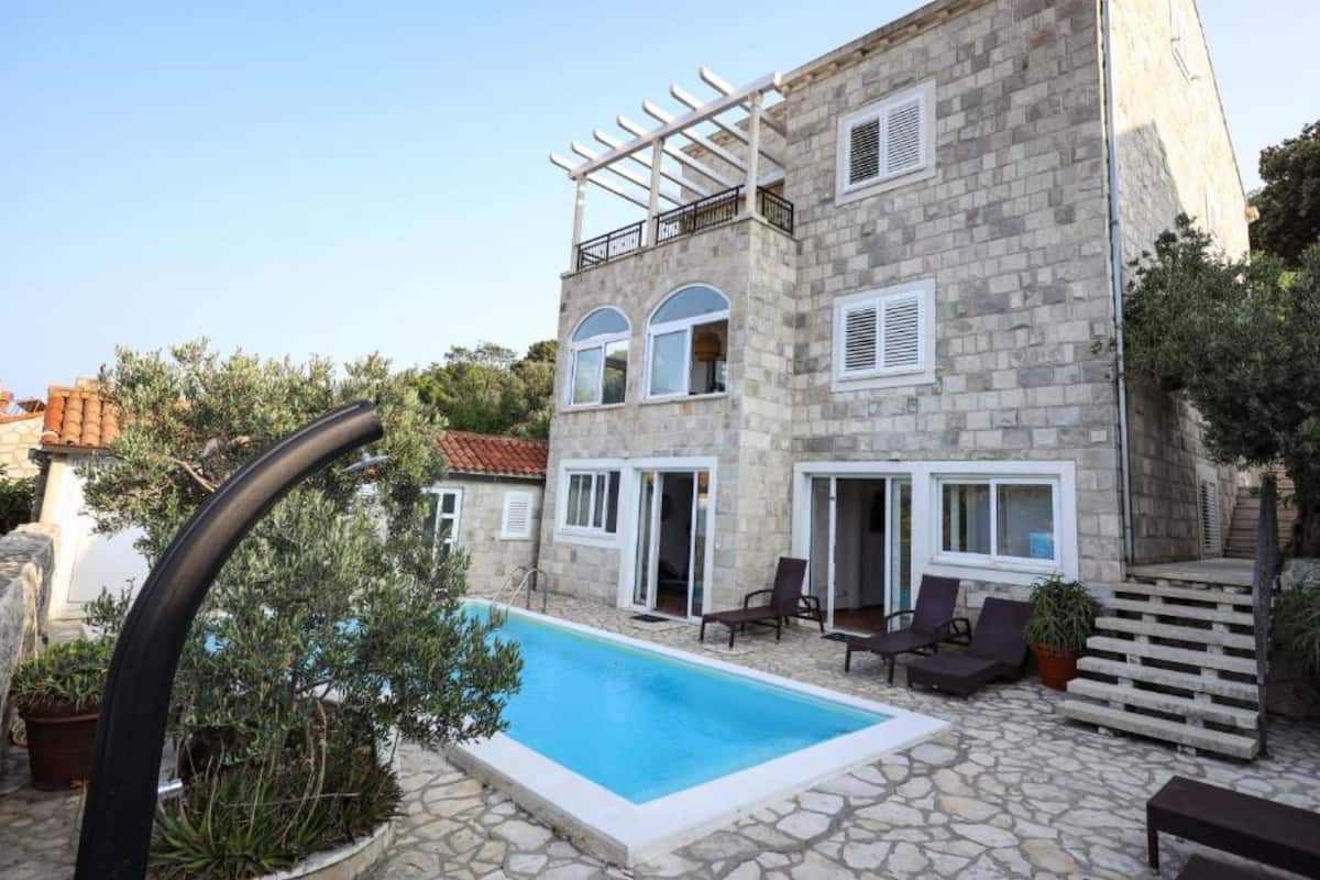 Un bâtiment en pierre doté d’une piscine, d’un espace extérieur aménagé et d’une pergola.