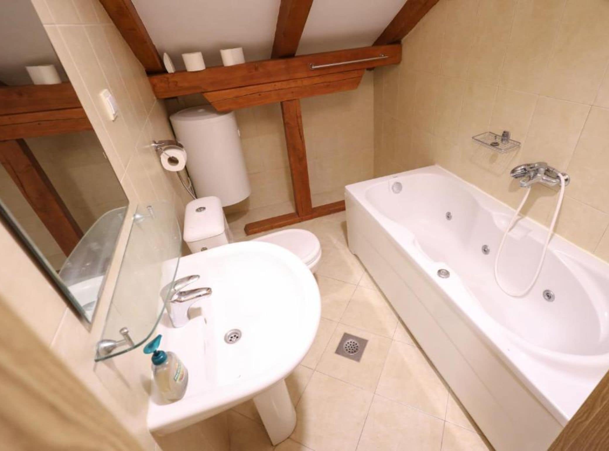 Un baño con bañera, inodoro, lavamanos y vigas de madera en el techo.