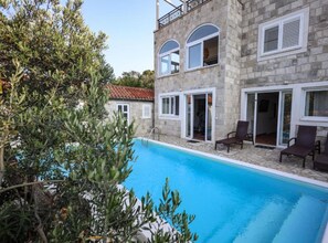 A two-story stone building with a swimming pool, outdoor seating, and a balcony.