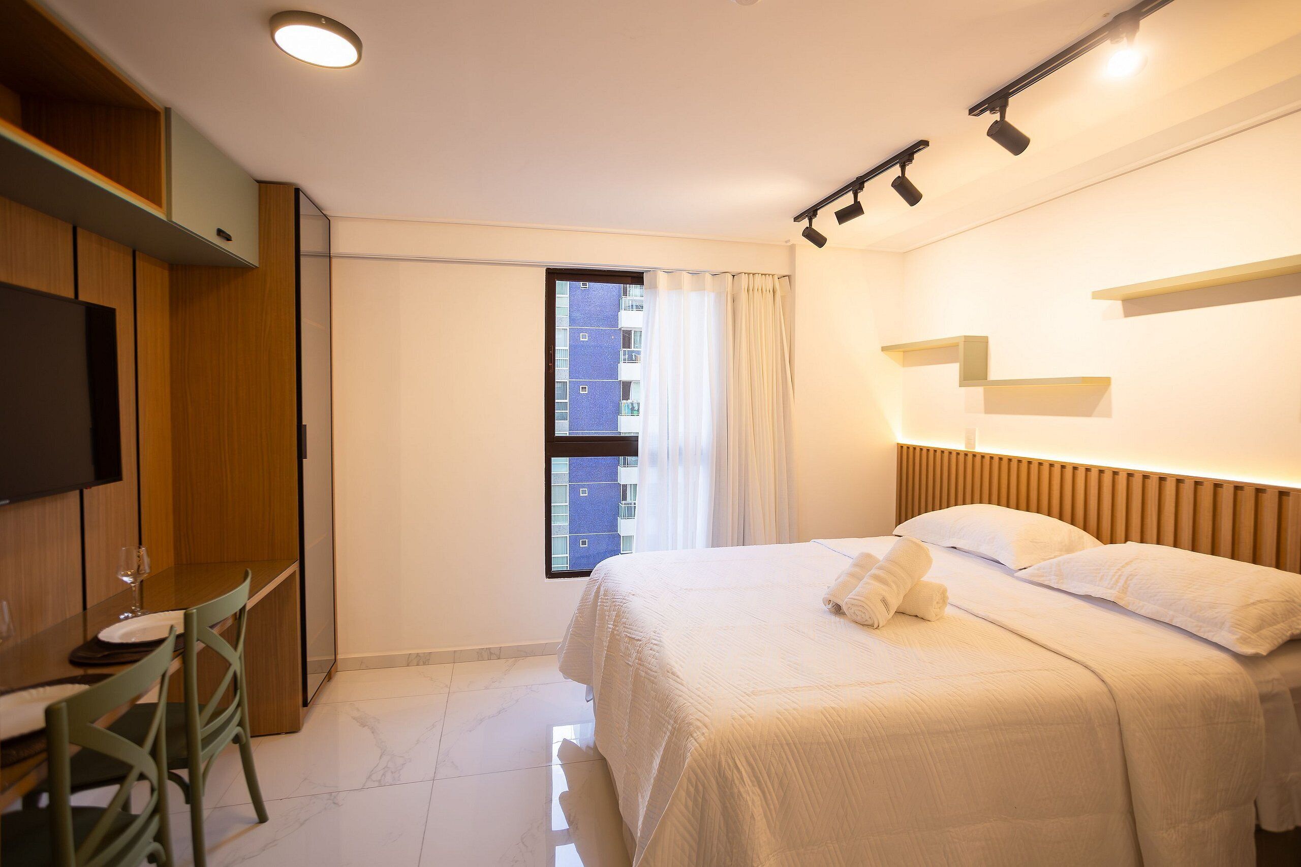 Habitación de hotel con cama, escritorio, silla, televisor y ventana con cortinas.