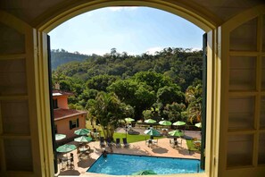 A pool with umbrellas, lounge chairs, and a view of a forested hillside. - HOTEL SOLAR FAZENDA DO CEDRO (Areal)