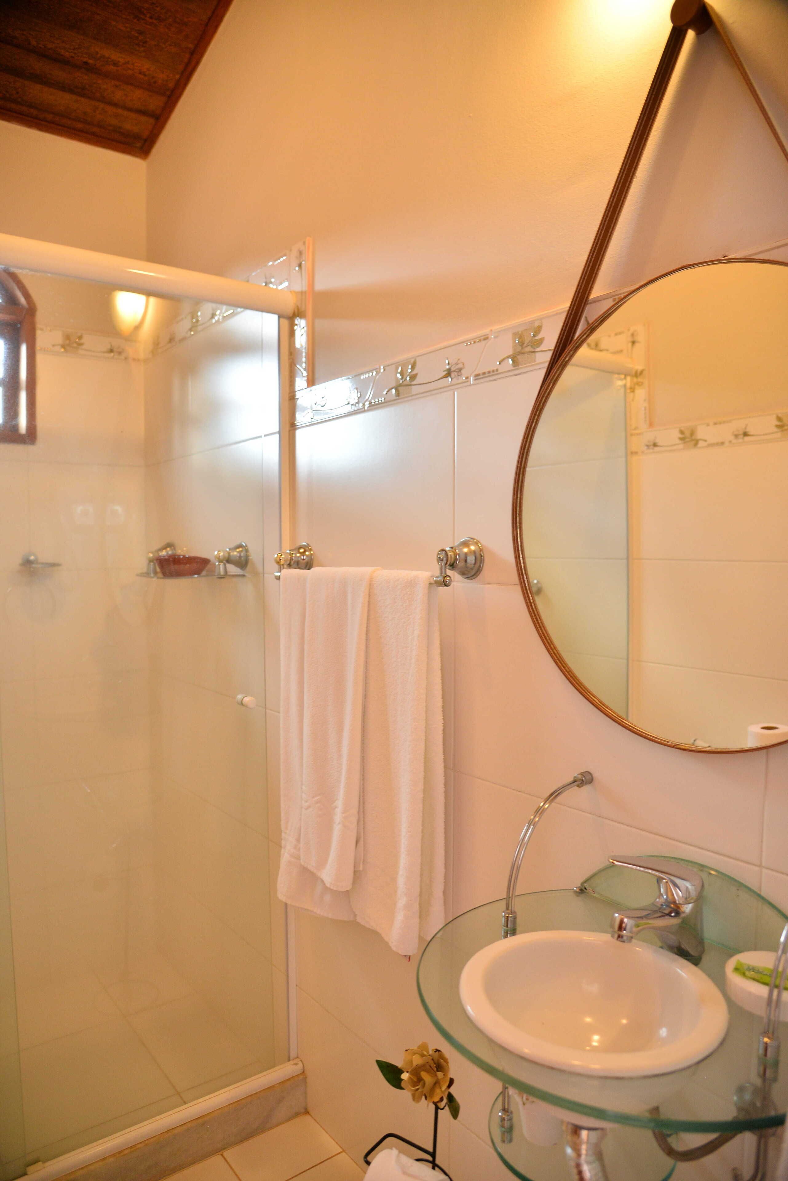 Un baño con lavabo de vidrio, un espejo redondo, cabina de ducha con paredes de vidrio y un perchero.