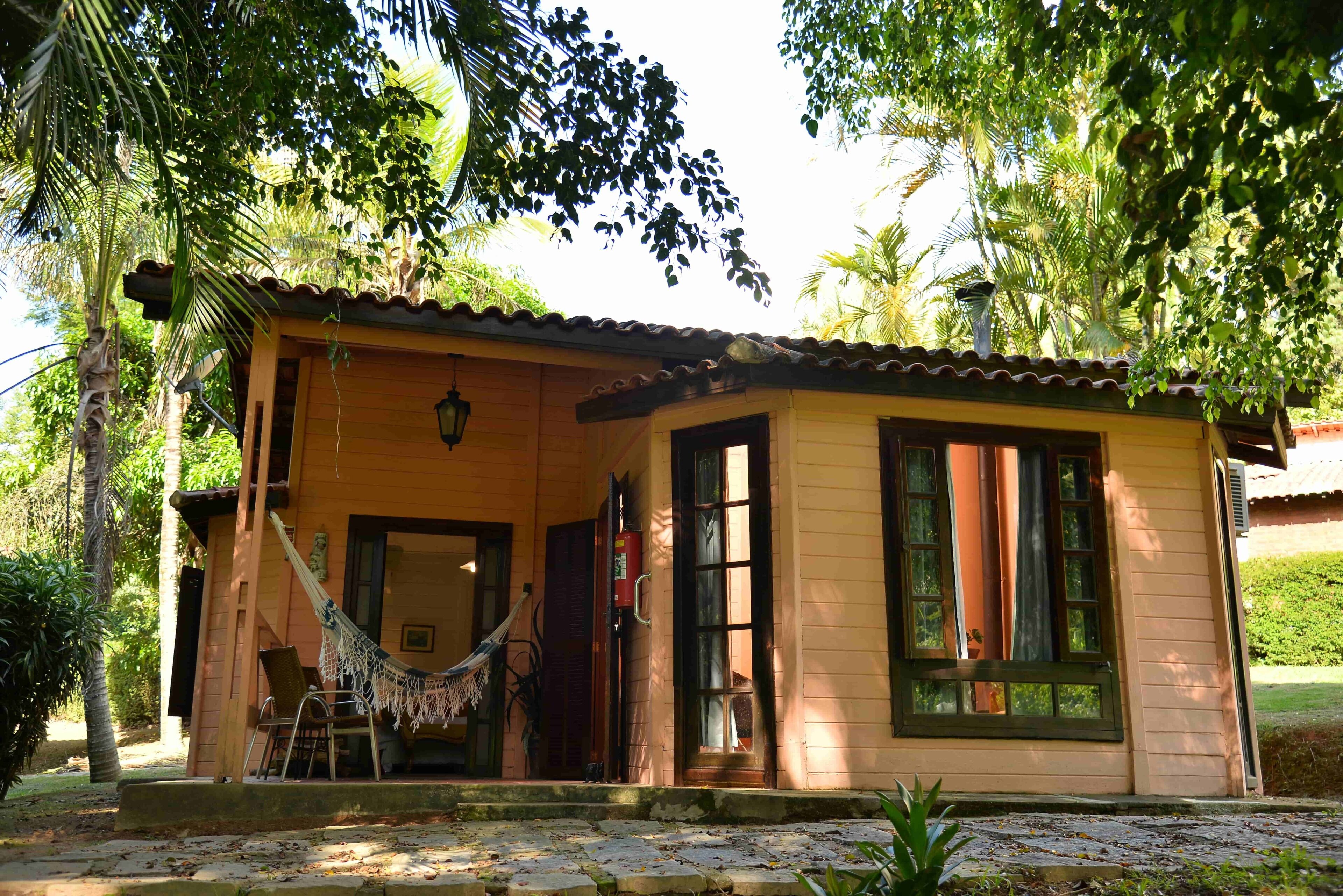 A small, single-story building with a tiled roof, a hammock, and a chair outside.