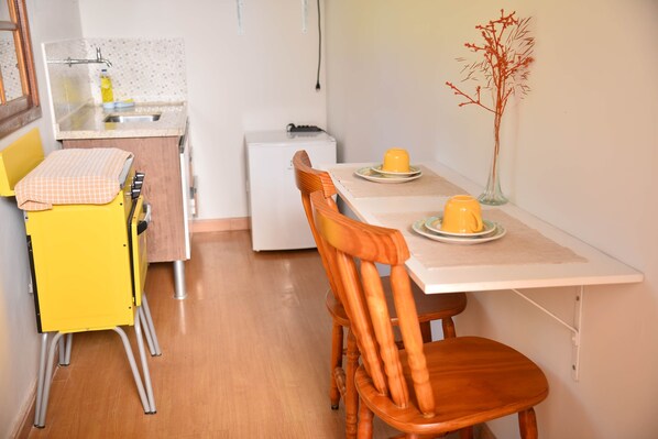 A compact kitchen with a dining table, chairs, a small refrigerator, and a vase with dried branches.