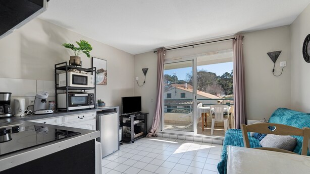 A modern kitchen with a built-in stove, microwave, and coffee maker. There is a balcony with a sliding door and a view of the outside. - Golf Apartment - Pornic 2 with Shared Pool, Balcony and Wi-Fi (Pornic)