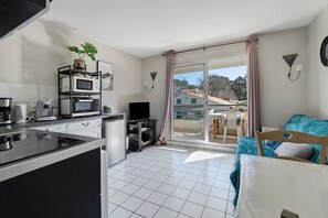Une cuisine moderne équipée d’une cuisinière intégrée, d’un four à micro-ondes et d’une machine à café. Un balcon avec une porte coulissante offre une vue sur l’extérieur.
