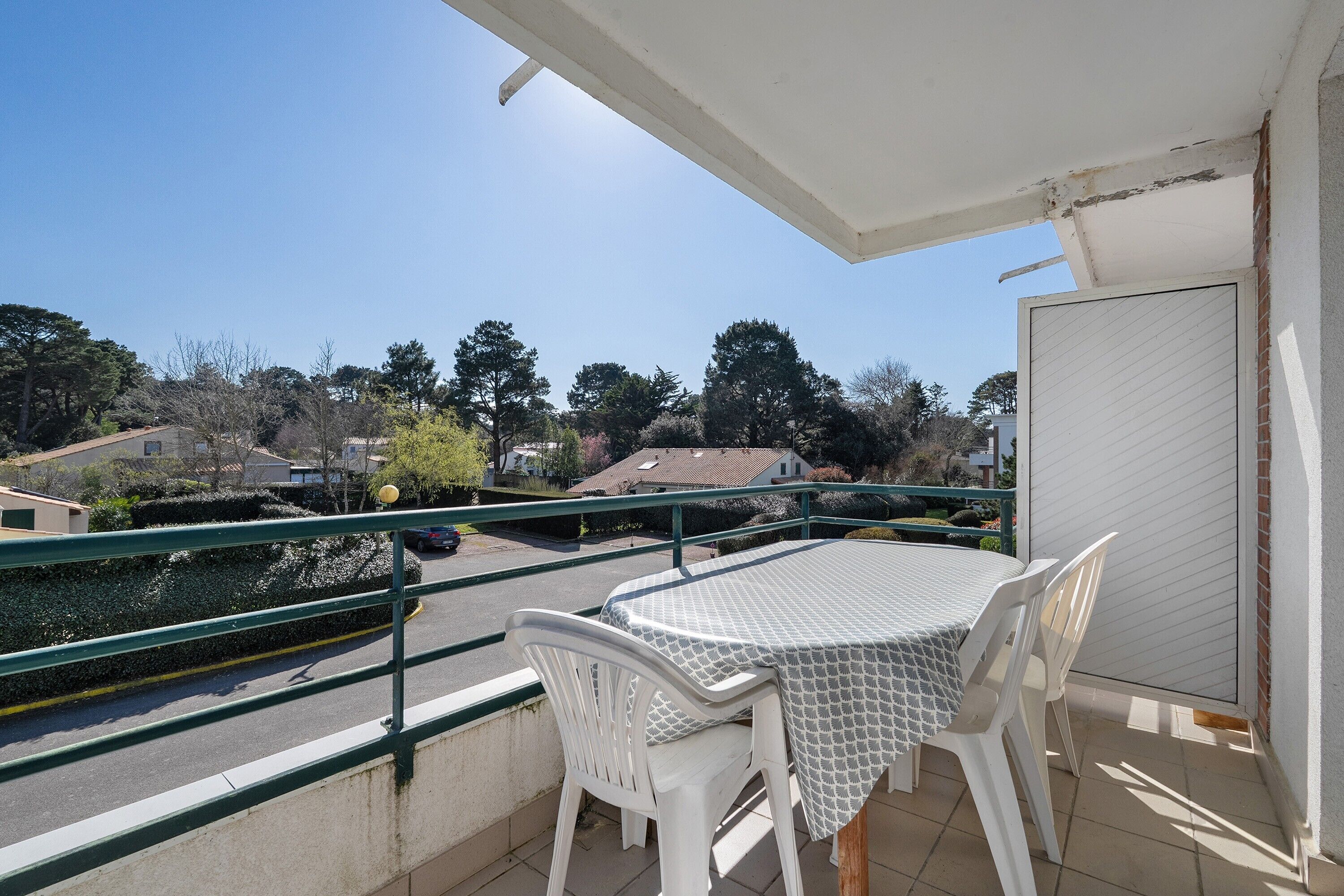 A balcony with a table and chairs, a view of the street, and a door.