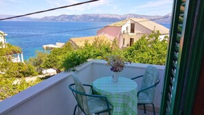 Un balcon avec une table et des chaises, donnant sur une étendue d’eau et sur des montagnes lointaines.