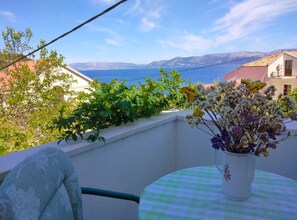 A balcony with a view of the sea, a potted plant, and a table with a checkered tablecloth. - Guest House Hazdovac Apartment (Mljet)