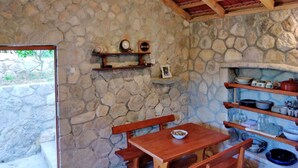 Une cuisine aux murs de pierre, avec des bancs en bois, des étagères remplies de vaisselle et un luminaire suspendu.