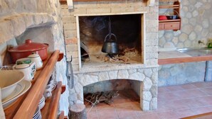 Une cheminée en pierre avec un pot suspendu, un pot rouge et une étagère contenant des ustensiles de cuisine.