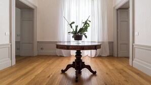 A round wooden table with a plant in the center, set against a white wall with a window and curtains. - Dimora Torremuzza historic home downtown Palermo with three bedrooms and 4 bathrooms (Palermo)