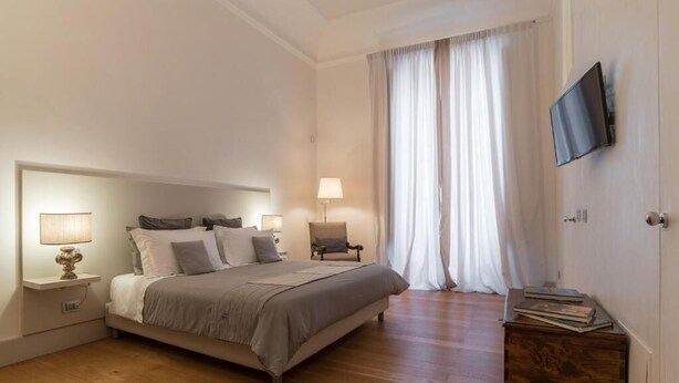 A bedroom with a bed, bedside tables, a lamp, a chair, a TV, and a wooden chest of drawers. - Dimora Torremuzza historic home downtown Palermo with three bedrooms and 4 bathrooms (Palermo)